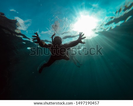 Underwater photo of men snorkeling in a deep blue tropical sea with sunrays in background