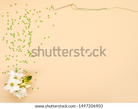 Hobby, craft, needlework or beading concept. Flat lay, top view. Creative minimalist background with space for text. Green glass beads, needle and thread decorated with white flower.