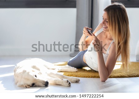 Shot of pretty young woman taking photographs to her dog while staying on the floor at home.