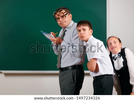 Portrait of a teacher checking homework, reading school exercise books, schoolboy and schoolgirl with old fashioned eyeglasses posing on blackboard background - back to school and education concept