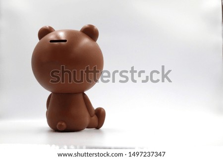 Brown bear shaped piggy bank sitting back left side on white background 