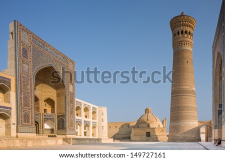 Exterior of Mir-i-Arab Medressa and Kalon Minaret. Two tourists are sitting at the entrance to Kalon Mosque. Photo taken in Bukhara, Uzbekistan.
