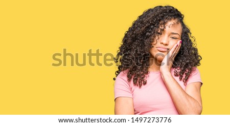 Young beautiful woman with curly hair wearing pink t-shirt thinking looking tired and bored with depression problems with crossed arms.