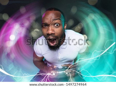 Passioned for winning. Young man holding a video game controller isolated on colorful background. Full of emotions. Leisure activity. Trying to reach the highest level but has the worst team ever.
