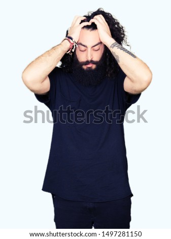 Young man with long hair and beard wearing heavy metal black outfit suffering from headache desperate and stressed because pain and migraine. Hands on head.