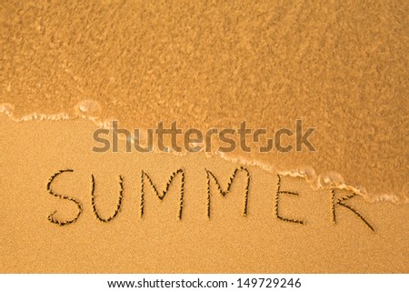 Summer, text written by hand in sand on a beach, with a soft wave.