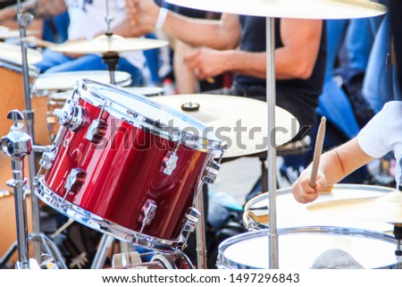 Street music band plays on various drum kits. They perform outdoor at summer day. Red color drumset and boy hand close up shot