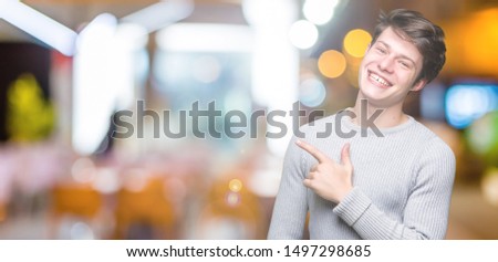 Young handsome man wearing winter sweater over isolated background cheerful with a smile of face pointing with hand and finger up to the side with happy and natural expression on face
