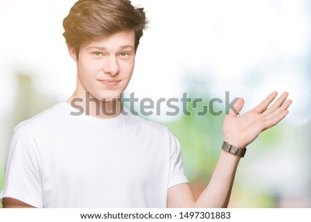 Young handsome man wearing casual white t-shirt over isolated background smiling cheerful presenting and pointing with palm of hand looking at the camera.