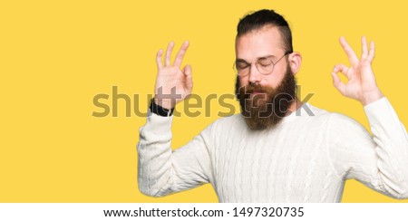 Young hipster man wearing glasses and winter sweater relax and smiling with eyes closed doing meditation gesture with fingers. Yoga concept.