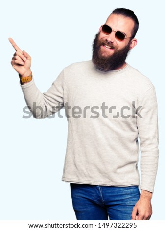 Young hipster man wearing sunglasses with a big smile on face, pointing with hand and finger to the side looking at the camera.