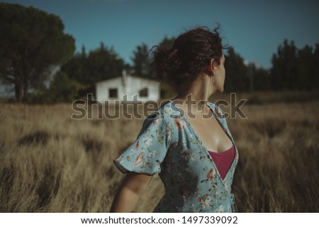 Woman in the field looks back with a house in the background