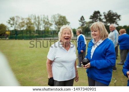 A front view shot of two senior women smiling at a bowling green.