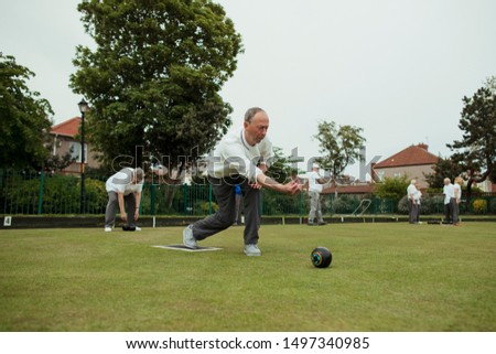 A front view shot of a senior man taking his shot in a game of lawn bowling.