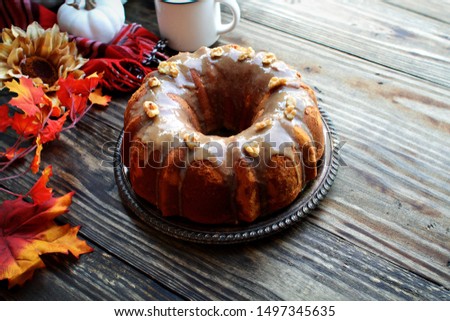 Delicious, Pumpkin Spice Bundt Cake frosted with brown sugar frosting and walnuts with Autumn leaves and coffee over a rustic wooden table background. Image shot from above. Fall foods.
