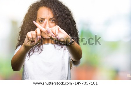 Young beautiful girl with curly hair wearing casual white t-shirt Rejection expression crossing fingers doing negative sign