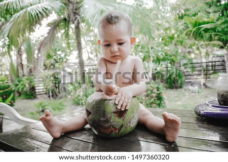 A small one-year-old child thoughtfully plays with the symbol of Halloween. Using coconut instead of pumpkin