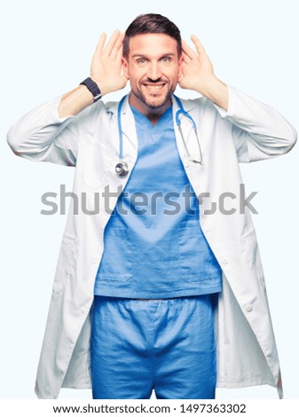 Handsome doctor man wearing medical uniform over isolated background Trying to hear both hands on ear gesture, curious for gossip. Hearing problem, deaf