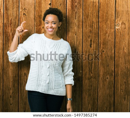 Beautiful young african american woman wearing sweater over isolated background smiling and confident gesturing with hand doing size sign with fingers while looking and the camera. Measure concept.