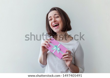 Young positive woman holding small pink gift box isolated on white background. Preparation for holiday. Girl looking happy and excited. Christmas birthday valentine celebration present concept