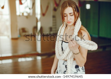 A stylish long-haired girl wearing a black and white sports suit training with white rope in a gym