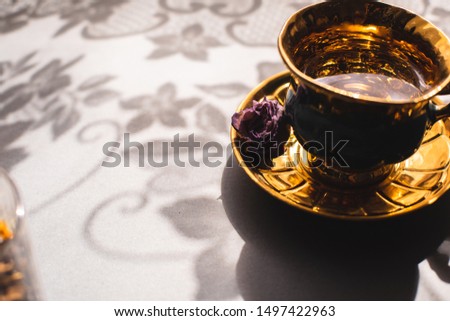 Vintage gold and green cup and saucer. Bright background with floral shadow. Good morning. Cup with water and eustoma flower. Copy spaces.