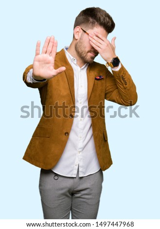Young handsome business man wearing glasses covering eyes with hands and doing stop gesture with sad and fear expression. Embarrassed and negative concept.