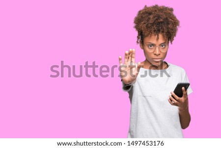 Young african american woman using smartphone over isolated background with open hand doing stop sign with serious and confident expression, defense gesture