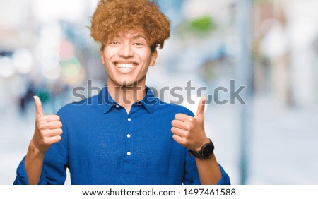 Young handsome elegant man with afro hair success sign doing positive gesture with hand, thumbs up smiling and happy. Looking at the camera with cheerful expression, winner gesture.