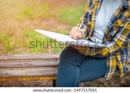 Woman in shirt sit and writing on an blank notebook with a pen. 