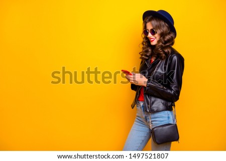 Profile side photo of cute sweet cheerful girl use her cellphone share post social network read feednews wear good black outfit denim jeans isolated over yellow color background