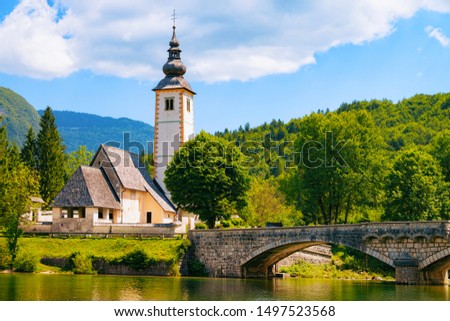 Scenery of Church of St John Baptist on Bohinj Lake at Slovenia. Nature in Slovenija. Blue sky with clouds. Beautiful landscape in summer. Alpine Travel destination. Julian Alps mountains. Mixed media