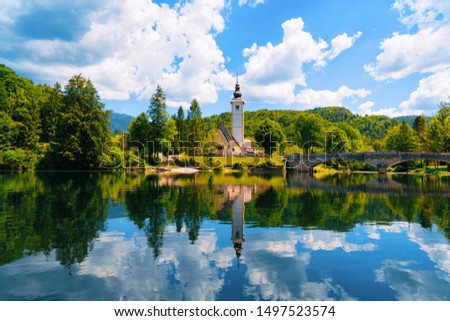 Scenery and Church of St John Baptist on Bohinj Lake at Slovenia. Nature in Slovenija. View of blue sky with clouds. Beautiful landscape in summer. Alpine Travel destination. Julian Alps mountains