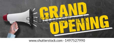 hand holding megaphone or bullhorn against chalkboard with text GRAND OPENING