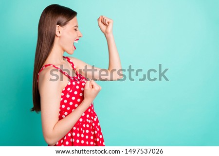 Profile side photo of cheerful lady with her eye closes raising fists screaming yeah wearing polka dot dress isolated over green teal turquoise background
