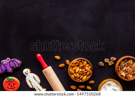 Cooking halloween cookies in shape of spooky figures, rollin pin, nuts and flour on black background top view mock up