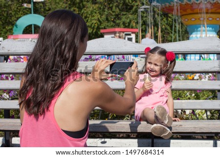 Mom takes pictures of her daughter in the park on a smartphone