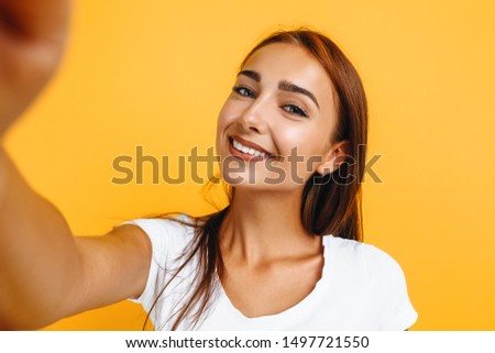 Young attractive girl takes selfie and smiles on yellow background