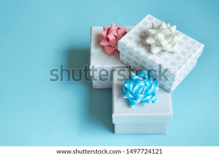 Three light gray gift boxes with light bows on blue background. Festive concept.