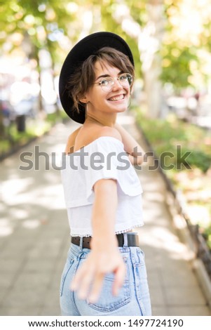 Smiling young woman walking outdoors, waving her hand