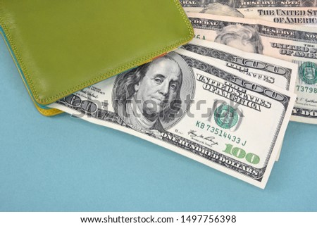 Hundred-dollar bills peek out of a green leather wallet on a turquoise background.