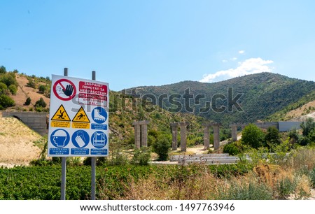 An unfenced building site with concrete columns ready for an elevated road in rural North Macedonia subsided by the European Union. A prominent no admittance sign warns of hazards and protective hats.