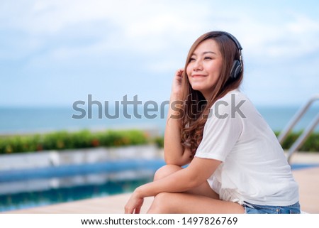 A beautiful asian woman listening to music  with headphone while sitting by swimming pool