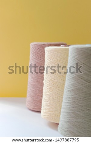 Pastel color bobbins of wool yarn for hand and machine knitting on a yellow background. Royalty-Free Stock Photo #1497887795