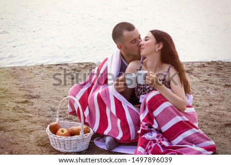 couple in love sitting wrapped in a plaid on the beach, early autumn, picnic, lake, river