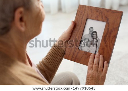 Elderly woman with framed family portrait at home