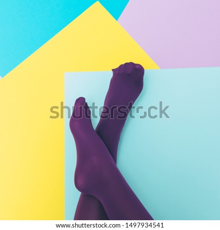 Women's legs in purple tights on a geometric blue, yellow, pink backgrounds. Minimalism