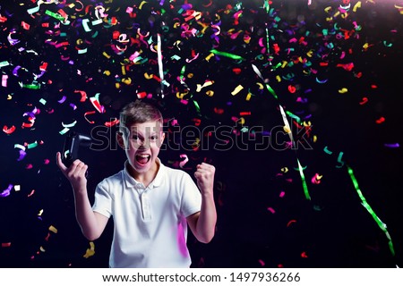 Cheerful kid with open mouth and joystick shouting for joy after winning in video game and colorful confetti falling on black background