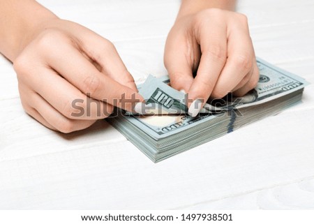 Perspective view of a businesswoman's hands counting one hundred dollar banknotes on wooden background. Success and wealth concept.