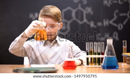 Little chemist observing reaction of orange liquid in flask, chemistry lesson